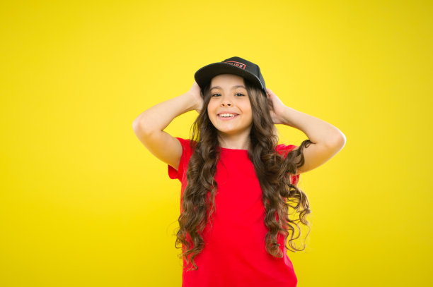 夏日防晒帽。女孩长卷发戴帽。一定要有街头时尚配饰的趋势。现代时尚。孩子们的时尚。可爱的孩子戴帽或snapback帽。戴着棒球帽的小女孩图片下载