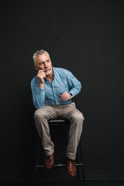 全长照片的白种男性退休60岁与灰色头发和胡子坐在椅子上看一边沉思的观点，孤立在黑色的背景图片下载