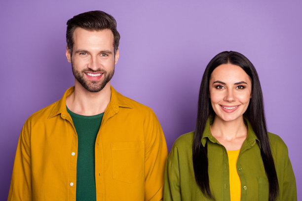 肖像照片漂亮的女士帅气的男孩学生夫妇站在一起牙齿微笑好心情快乐在一起穿休闲的黄色绿色衬衫孤立的紫色背景图片下载