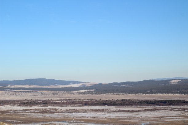 冬天，白雪皑皑的山上覆盖着松树林，黄澄澄的草地上覆盖着白雪，河面冻结，蓝色的夕阳映衬着黎明的天空图片下载