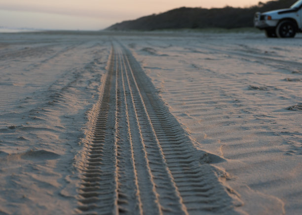 低角度照片的4x4轮胎履带在一个海滩上与车辆在背景图片下载