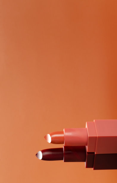 垂直的图像。两支开管的粉红色和深红色的口红映衬着橙色的背景。空的空间图片下载