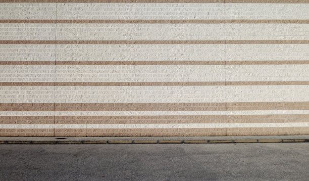 混凝土砌块墙以白色和棕色的水平条纹排列。前面是人行道和柏油路。图片下载
