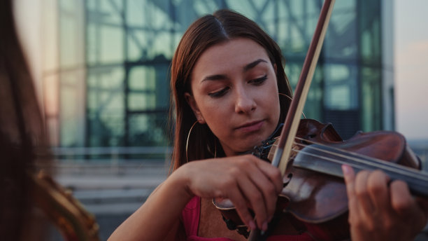 精力充沛的双胞胎姐妹享受屋顶音乐会议。在日落时演奏萨克斯管和小提琴图片下载