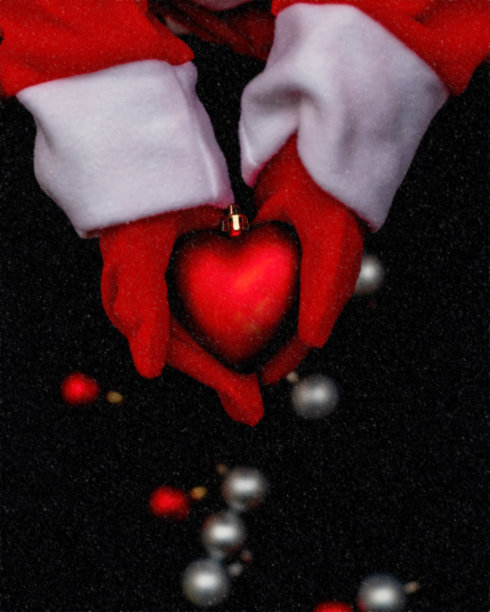 模糊的背景。戴着红色手套的手捧着心脏。圣诞老人手里拿着一个红色的圣诞树玩具，背景是黑色的。圣诞节,新年。副本的空间。图片下载