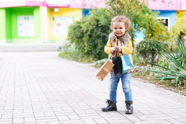 漂亮的小女孩拿着五颜六色的纸袋在户外购物图片下载