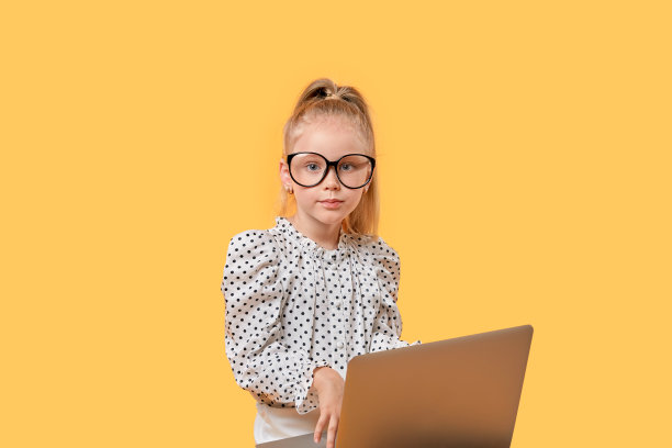 穿着圆点衬衫的可爱女孩看着镜头。旁边是一台打开的笔记本电脑。图片下载
