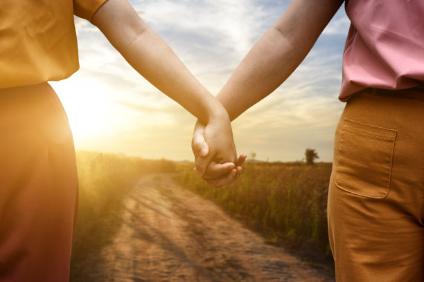 在夕阳的背景下，两名女性手牵着手走在路上。图片下载