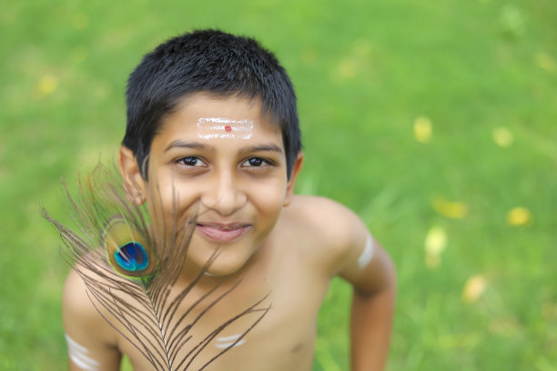 一个印度小孩手里拿着孔雀羽毛，装扮成奎师那神图片下载