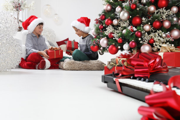 圣诞快乐，节日快乐，孩子们在圣诞树旁拿着乐器看礼盒，在家里客厅的地板上坐着图片下载