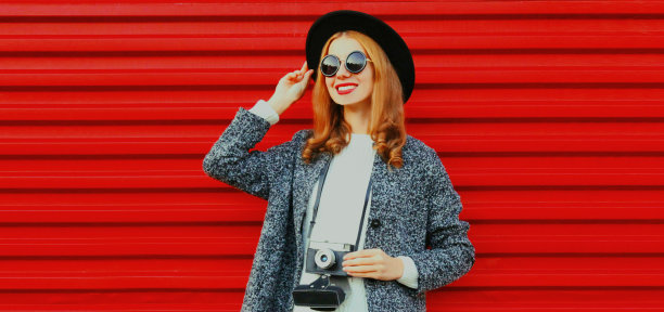 年轻女性摄影师与老式电影相机戴着黑色圆帽在红色背景图片下载