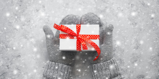 礼盒与红色丝带在女性手中在灰色的手套和毛衣，旗帜。俯视图，平放，复制空间。图片下载