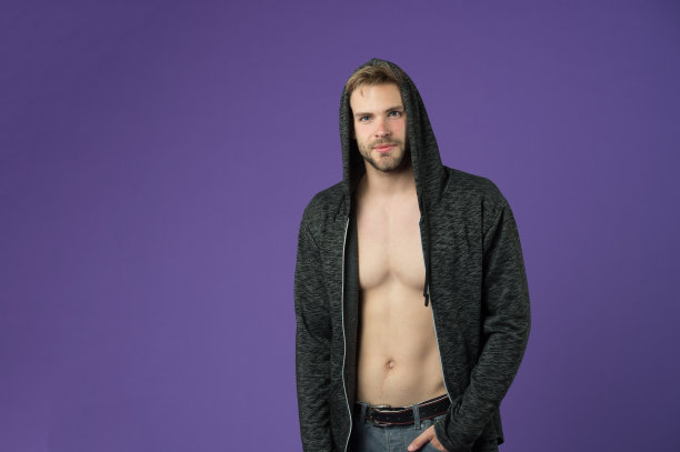男子与胡子戴兜帽在紫罗兰背景。男子与性感的躯干在休闲运动衫。穿着帽衫的时尚模特。积极的生活方式和健康活动。时尚风格与潮流概念，复制空间图片下载
