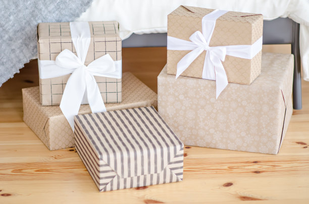 许多礼物用牛皮纸包着，用白色的丝带装饰着一个蝴蝶结，站在木地板上迎接圣诞老人。新年的奇迹。圣诞贺卡。副本的空间。纹理雪花图片下载