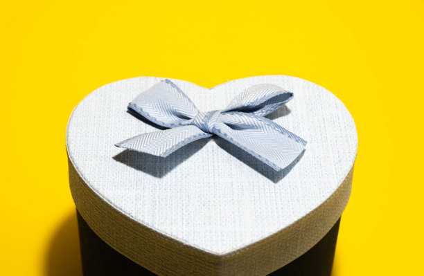 顶部有一个蓝色蝴蝶结的心形礼盒。蓝色礼品盒孤立在黄色背景上。特写照片。模糊。图片下载