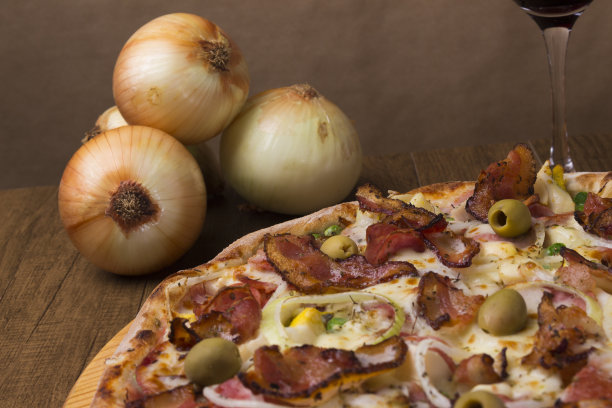 葡萄牙披萨，由火腿、豌豆蛋、棕榈心、意大利辣香肠、洋葱、马苏里拉奶酪和培根制成。用质朴的洋葱来构成这一场景。美食特写照片。图片下载
