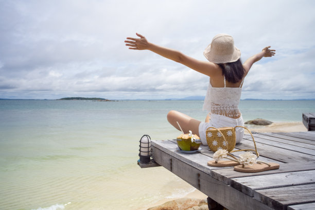 一个亚洲女人在一个晴朗的日子在海滩上喝椰子汁图片下载