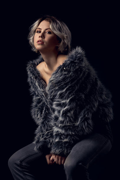 年轻女子奢华风格孤立地坐在灰色墙壁上的椅子上图片下载