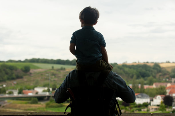孩子坐在他父亲的肩膀上，走在老城的街道上图片下载