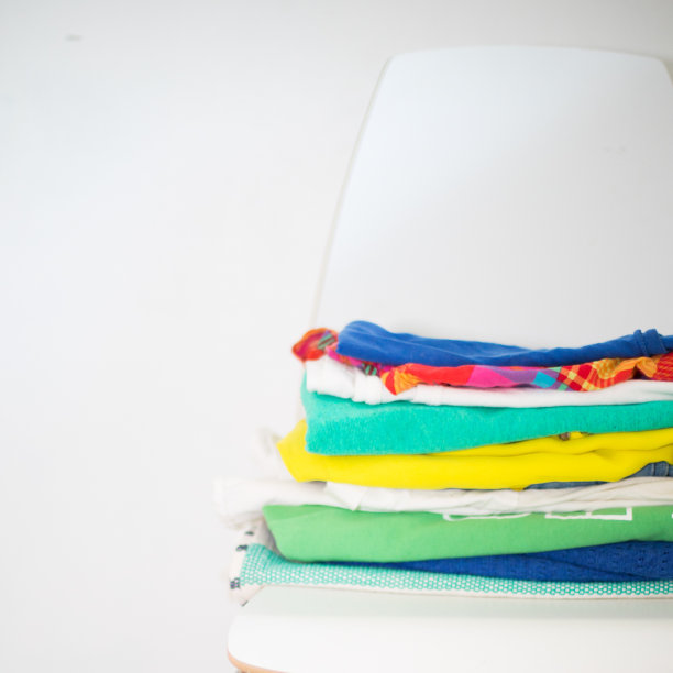 折叠的，彩色的衣服堆叠在白色背景的白色现代椅子上图片下载