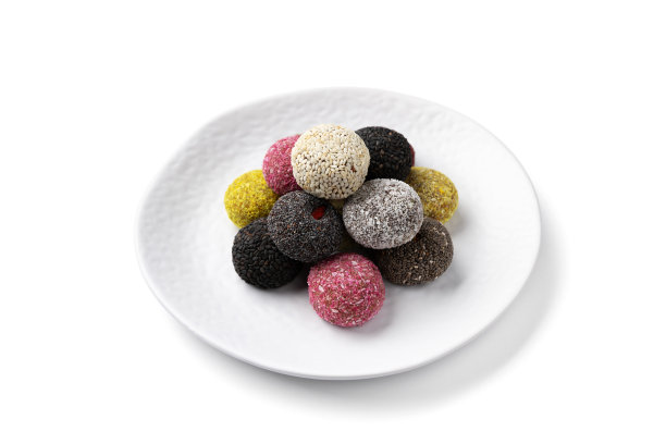 白色桌子上的盘子里放着五颜六色的素食糖果和能量球。图片下载
