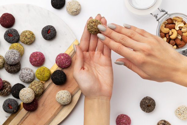 彩色素食糖果能量球在一个盘子与女人的手孤立的白色背景图片下载