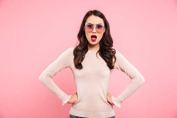 照片中愤怒的女人不经意地牵着手放在腰上，愤怒地看着镜头，在粉红色的背景下被孤立图片下载