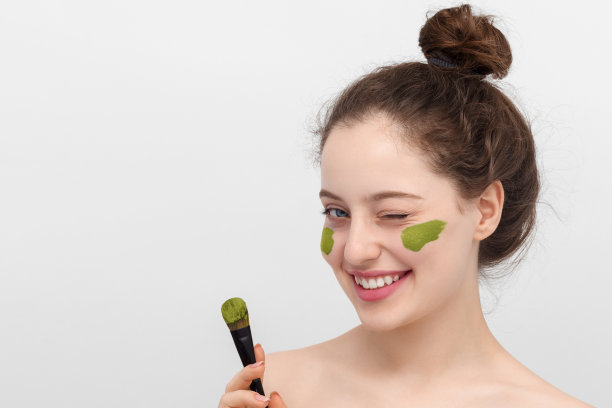 一名年轻女子将橄榄色面膜敷在脸上，手握刷子。图片下载