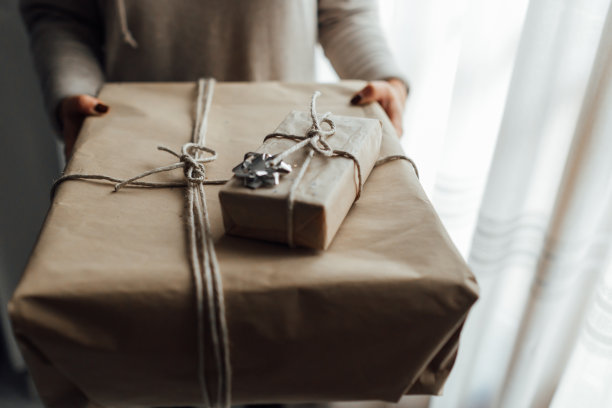 年轻女子手里拿着用牛皮纸和杜松树叠起来的圣诞礼品盒。圣诞礼物的概念。图片下载