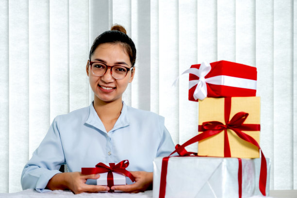 身穿蓝色衬衫的女子拿着一个用红色丝带系着的白色礼盒，礼物是为圣诞节、情人节等特殊节日准备的图片下载