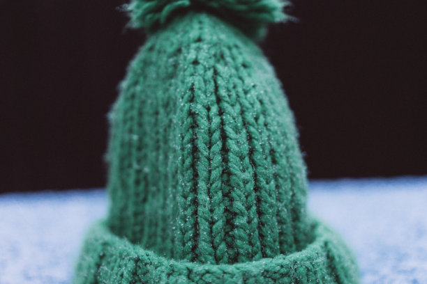 绿色编织的帽子上有一个绒球覆盖着雪，从雪滴下来，先湿雪，选择性对焦，胶卷和谷粒照片图片下载