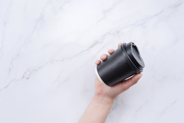 年轻女子手拿黑咖啡纸杯放在大理石桌上。图片下载