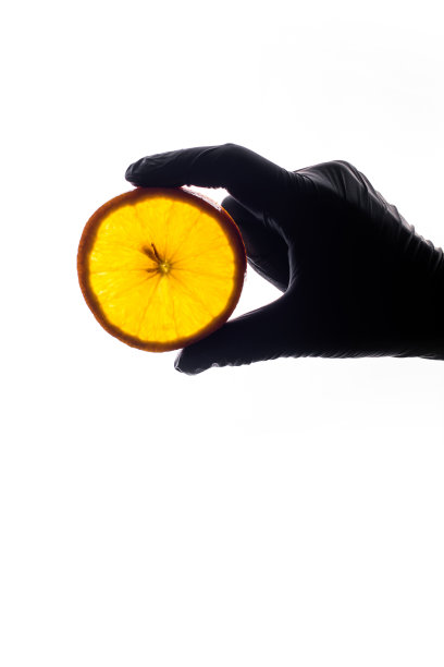 手在黑色手套拿新鲜的橙色切片在白色的背景。图片下载