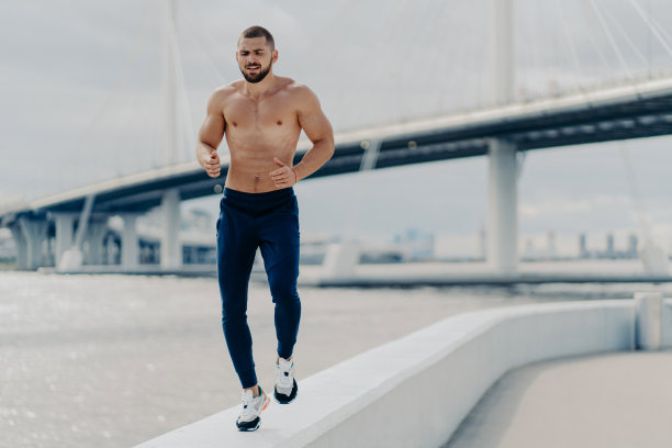 活跃的大胡子男性慢跑沿着河边跑步，在户外锻炼，穿着活跃的衣服准备运动比赛，有肌肉强壮的身体呼吸新鲜空气。运动生活方式概念图片下载