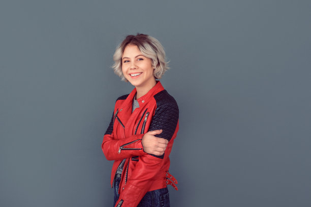 年轻女子穿着皮夹克，孤独地站在灰色的墙上，兴高采烈图片下载