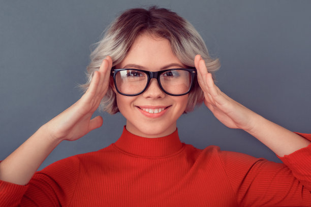 年轻女子身穿红色衬衫，戴着眼镜，孤立在灰色的墙壁上图片下载