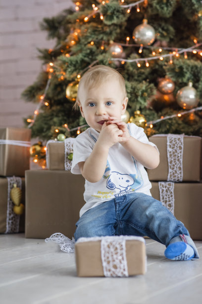 金发小男孩在家的圣诞树旁吃着姜饼人。新年贺卡与花环散科。宝宝笑了，打开了圣诞老人送的礼物盒。等待奇迹。本空间图片下载