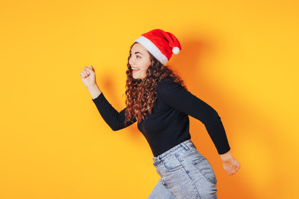 漂亮的女人穿着黑色的毛衣和红色的圣诞帽在她的头在黄色的背景图片下载