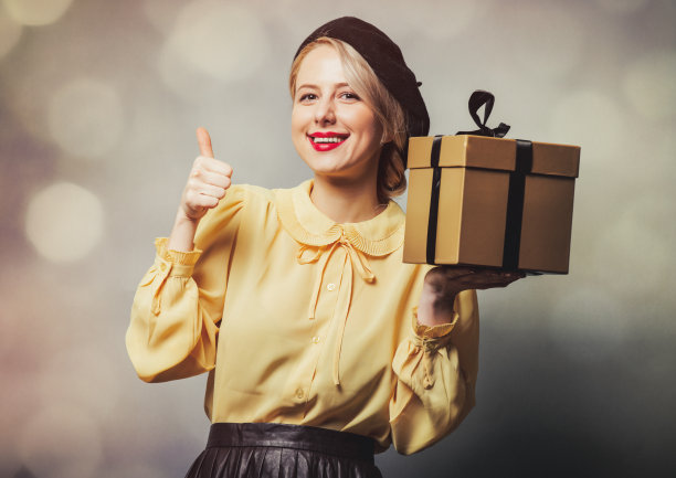 漂亮的女孩在复古的衣服与礼物的灰色背景图片下载