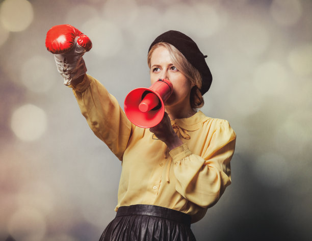 漂亮的女孩穿着复古的衣服，带着扩音器和拳击手套，灰色的背景图片下载