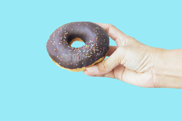 巧克力甜甜圈手拿孤立在蓝色背景图片下载