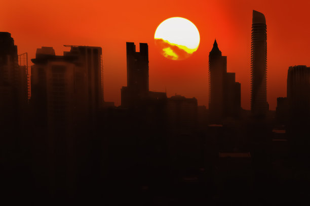 抽象戏剧性的摄影剪影在大城市摩天大楼与令人毛骨悚然的红橙色黄昏天空和大日落显示恶劣的环境和危险的天气。图片下载