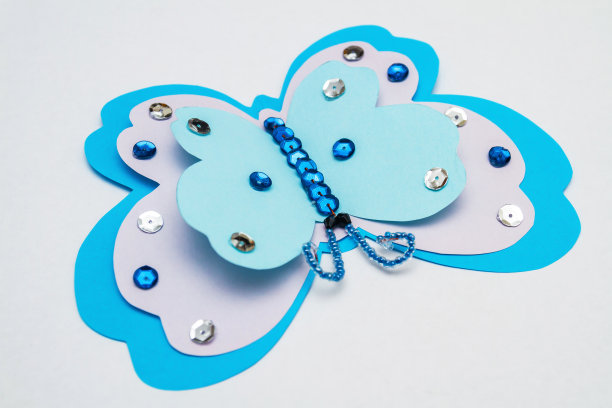 应用热熔胶枪。彩色纸做的蓝色蝴蝶，多色亮片，亮片和珠子。特写镜头,有选择性的重点图片下载