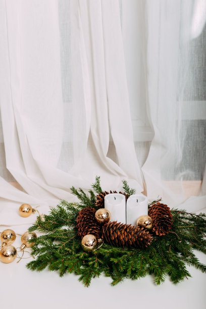 斯堪的纳维亚圣诞贺卡与白色织物和圣诞花环与白色蜡烛内。绿色的冷杉枝，松果，金色的球和蜡烛在白色的背景与文字的空间。图片下载