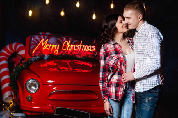 美丽的情侣在发光的灯光和复古的汽车背景下拥抱在一起。工作室肖像照片。情人节。爱的夫妻。情人节。圣诞假期图片下载