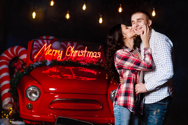 美丽的情侣在发光的灯光和复古的汽车背景下拥抱在一起。工作室肖像照片。情人节。爱的夫妻。情人节。圣诞假期图片下载