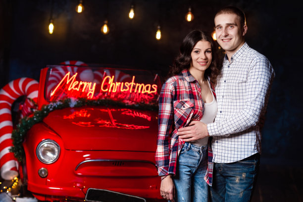 美丽的情侣在发光的灯光和复古的汽车背景下拥抱在一起。工作室肖像照片。情人节。爱的夫妻。情人节。圣诞假期图片下载