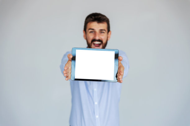 满脸胡须的商人微笑着站在白色背景前，手持平板电脑。有选择地专注于平板电脑。图片下载