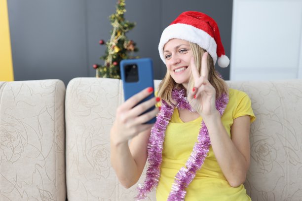 戴着圣诞老人帽的微笑女子看着智能手机，严肃地握着手指。图片下载