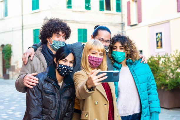 一群快乐的朋友戴着防护口罩在重开后的城市街道上自拍。多民族男人和一个女人在一个城市背景下自拍照片。新常态的生活方式图片下载